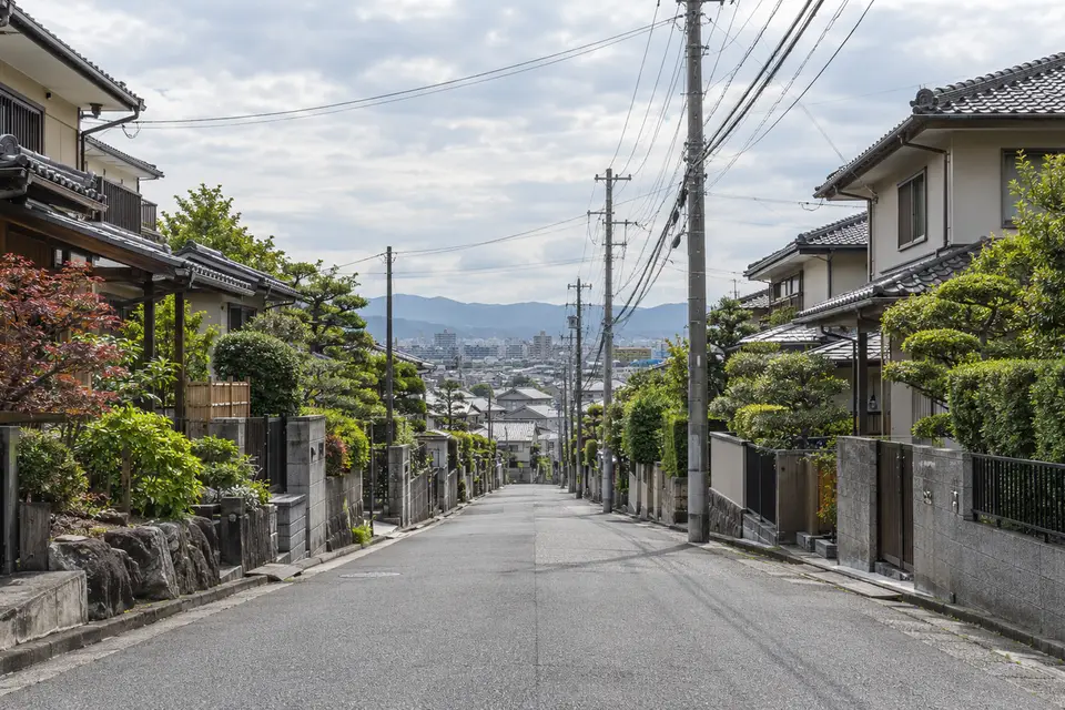 瓦屋根の戸建てが両側に並び、遠くの街へ続く坂道のある日本の住宅街
